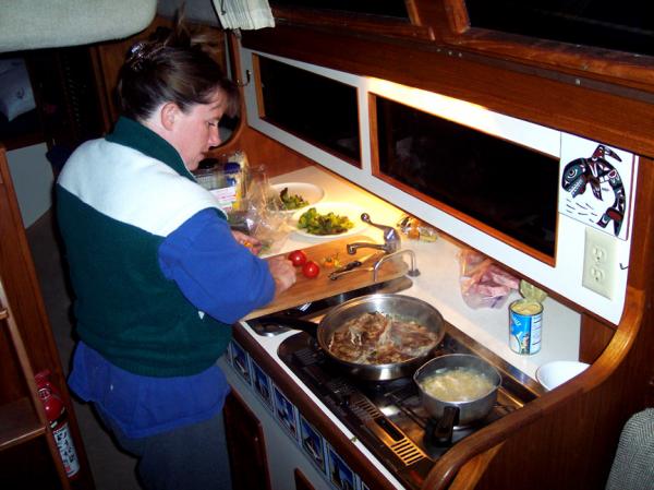 Catherine in the portside galley of AQUILA. Two burner alcohol stove, pressurized hot / cold water. Deep, segmented ice box. Directly aft is the nav station.