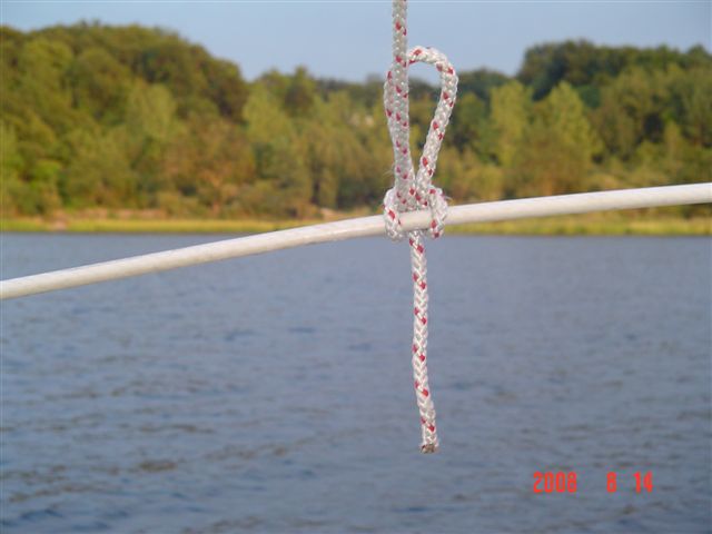 DSC01121 I have about three or four of these lines going to my lifelines from the tarp.  The hitch pictured is a slipped Clove Hitch.  These hitches are so simple to tie that I can do them with my right hand.  You can trip this hitch by pulling on that line hanging down.
Once you get to hanging these tarps you get to where you can do it without even thinking.  It becomes automatic.  
 We went through two strong gales in one day last year while anchored with this tarp and it survived it with no rips.