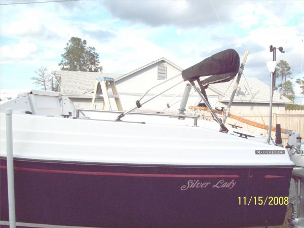 Portside.  Cockpit rails effectively raised low seatbacks. Bimini top on slide mount.  Anomometer and GPS antena on stern post. Rod holders on side rails.  large stern cleats.  New tiller. Tiller tamer. Note angled lifeline that ended just past boarding step (tripper) moved to cabin top.