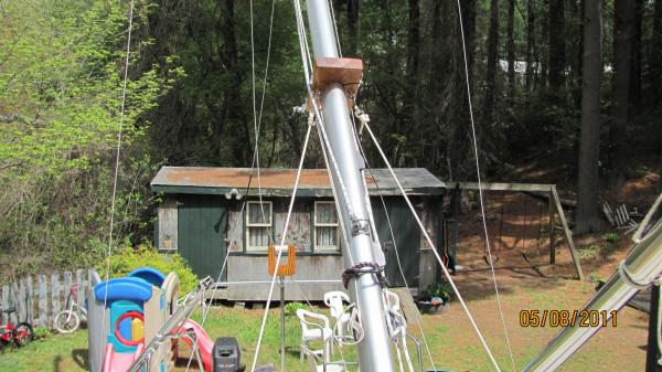 This gadget is clamped to my mast and it's main function is to keep the mast from going over the side as I raise/lower.  I call it a mast yoke and there are temporary stays (baby stays) connected to it and pivot bridles on both sides of my boat located on the side decks near the chainplates.  

 There are two simple rules to follow when raising/lowering the mast from the stern of the boat:  1.  Always make sure that the boat is level from side to side.   2. The wind needs to be coming directly from aft.     If the boat is leaning to one side, the temporary stays may not support the mast.  The same holds true if a large gust of wind hits the mast from the beam of the boat while raising/lowering.   In either case the mast can go over the side.  
If you don't have a furler, the mast yoke along with temporary stays and pivot bridles can be omitted as long as you follow those two simple rules.     All that is needed is the Gin pole and the mast crutch in the stern.